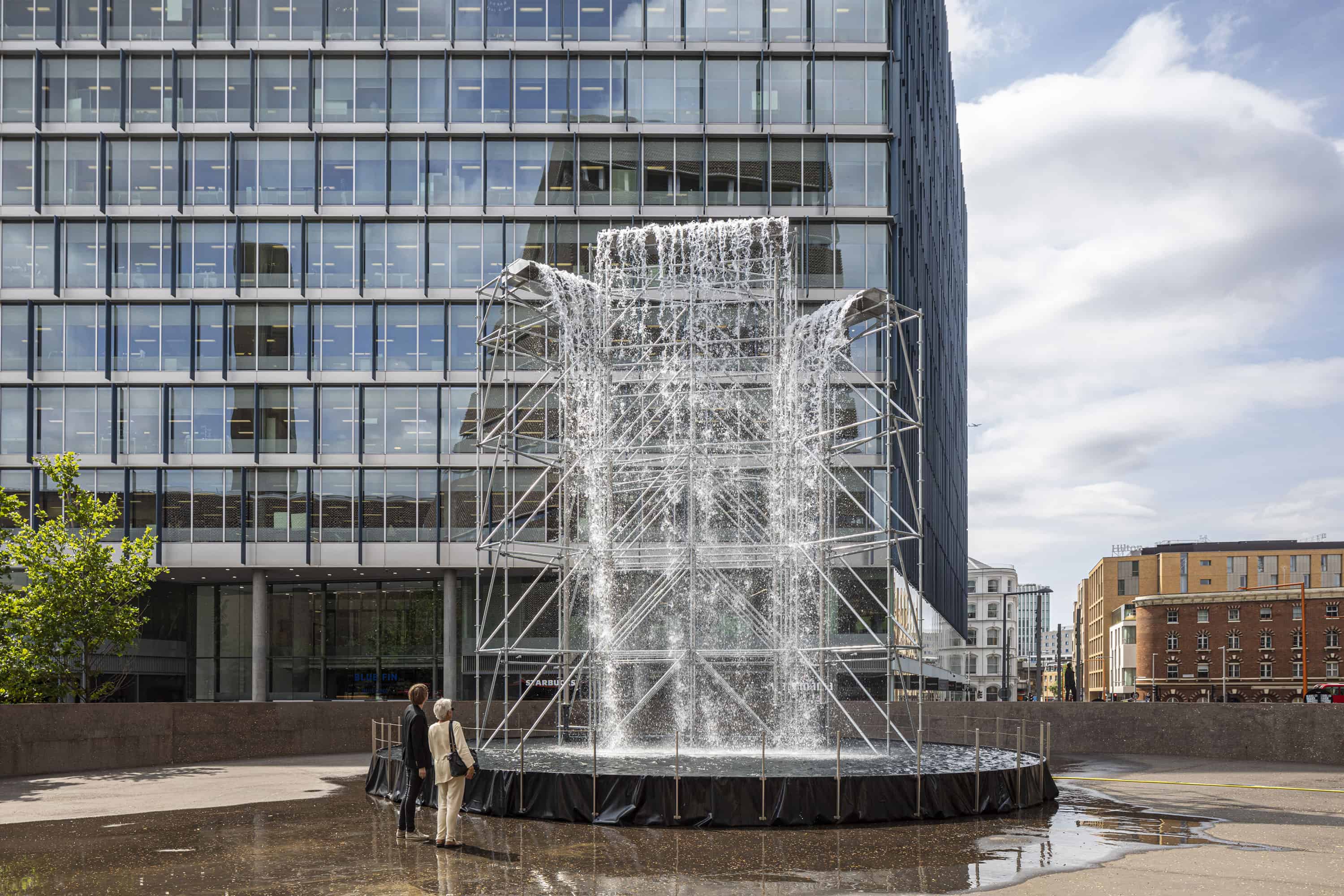 Olafur Eliasson, Waterfall, 2019, Scaffolding, water, wood, plastic sheet, aluminium, pump, hose, Height 11 metres, diameter 12 metres, Courtesy the artist; neugerriemschneider, Berlin; Tanya Bonakdar Gallery, New York / Los Angeles, Installation view: Tate Modern, London, Photo: Anders Sune Berg, © 2019 Olafur Eliasson