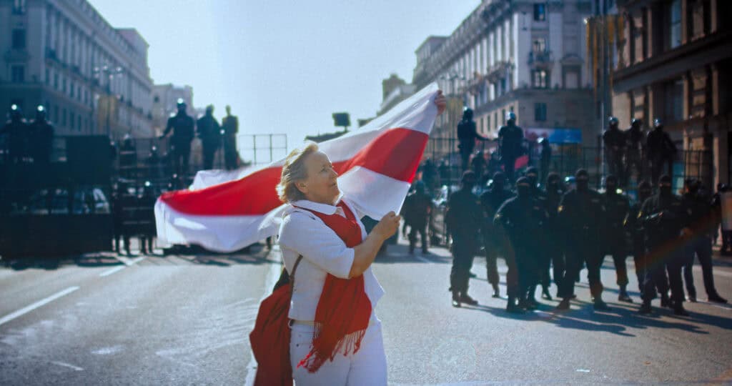 COURAGE, copyright: Living Pictures Production Demonstrantin mit belarussischer Fahne vor einer Absperrung von Spezialeinheiten des Regimes. Sonntagsmarsch am 30.08.2020 in Minsk.