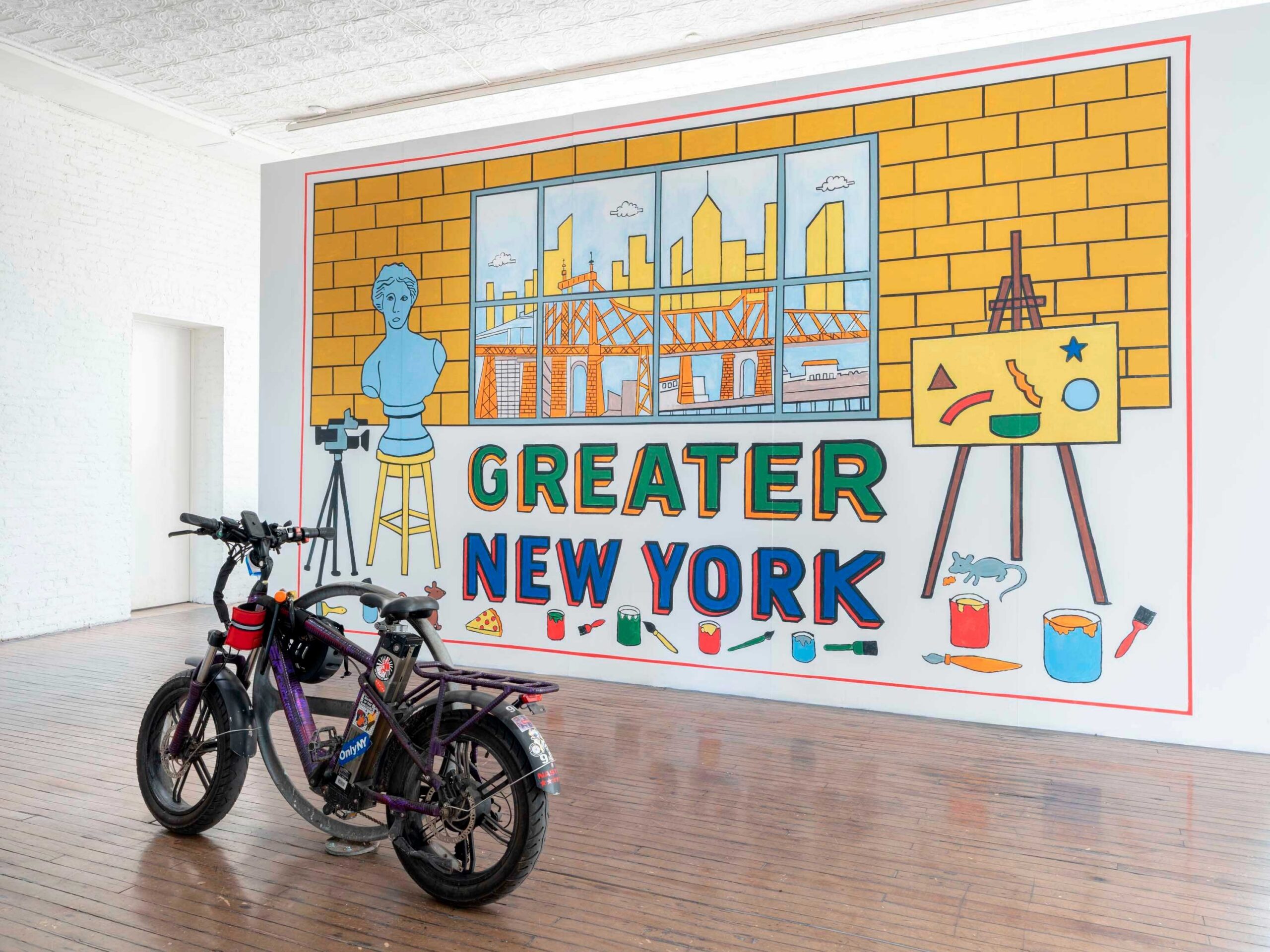 Left: fields harrington. Unfree Free Time (Bike Rental). 2026. E-bike and bike rack. Right: Cevallos Brothers. Greater New York. 2026 Acrylic on wall. Installation view of Greater New York, on view at MoMA PS1 from April 16 through August 17, 2026. Courtesy MoMA PS1. Photo: Kris Graves